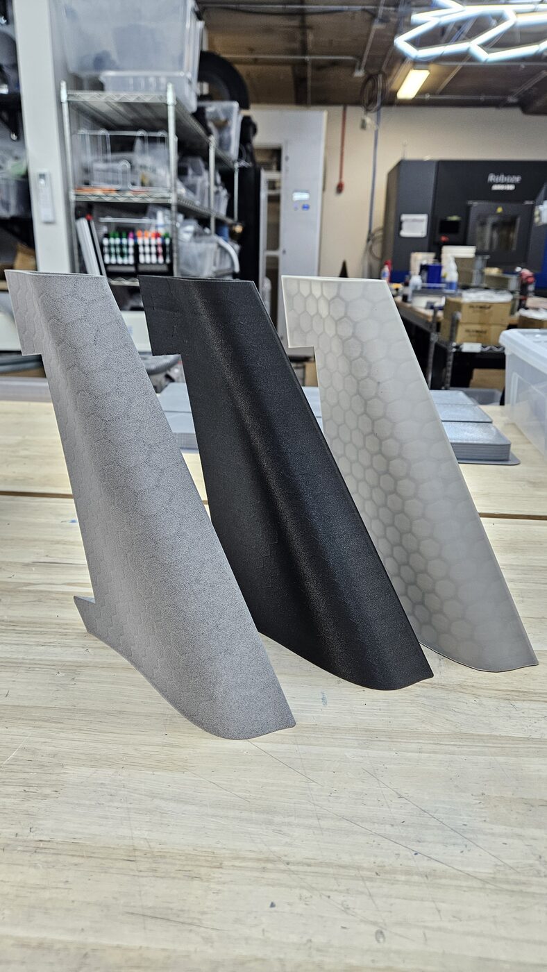 Three drone airframe panels printed in different material finishes side by side